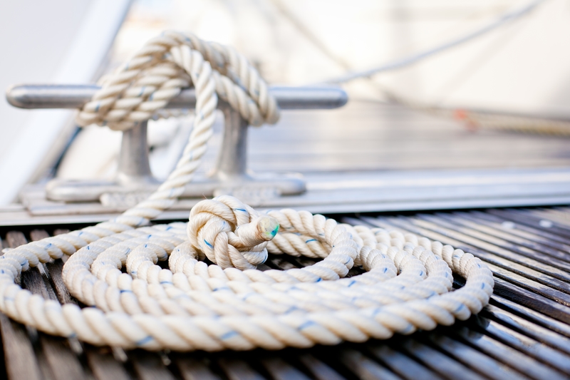 Coiled white rope beside a cleat on a teak deck